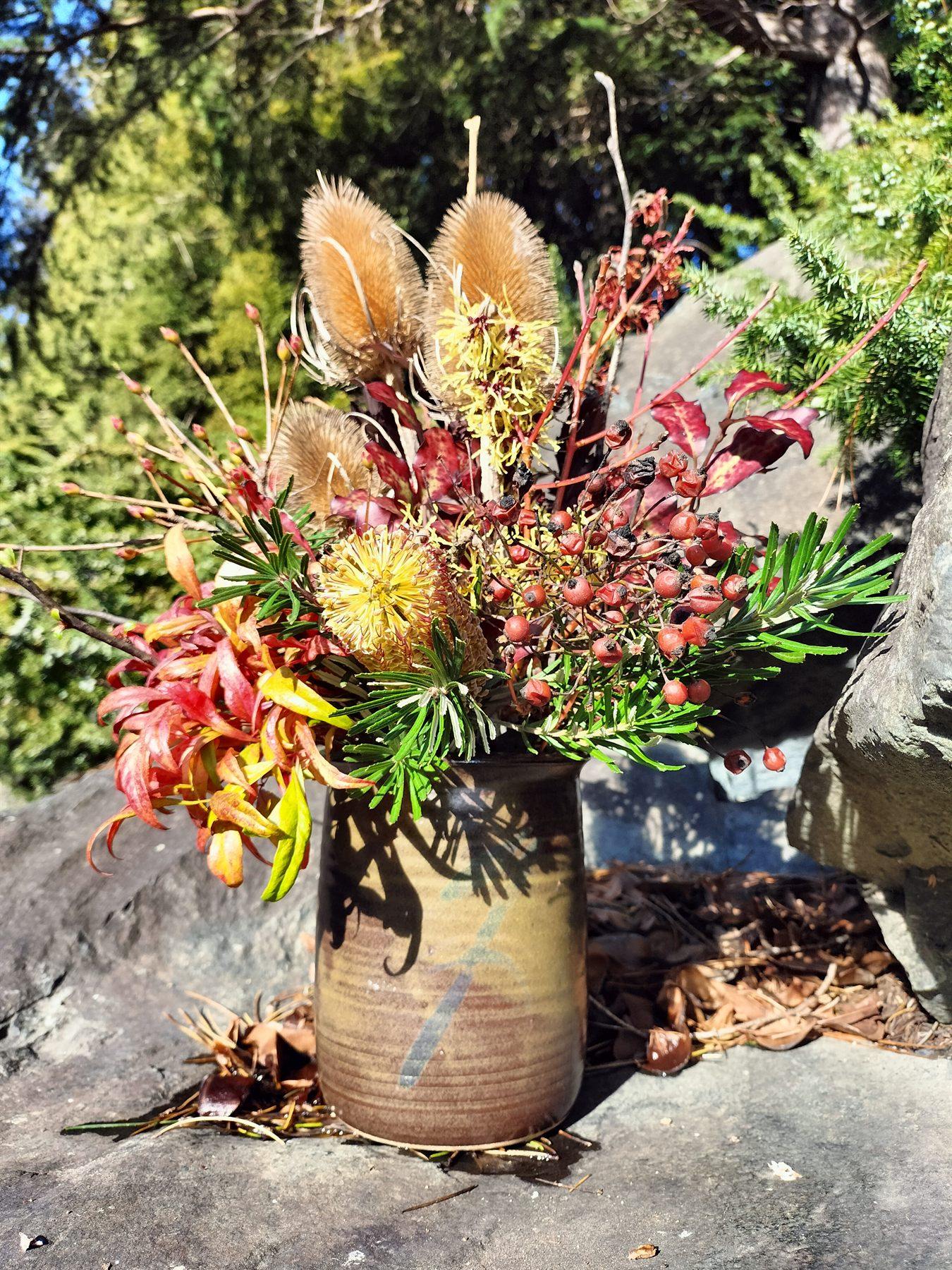 A flower arrangement of garden foliage and seed heads in a stoneware jar